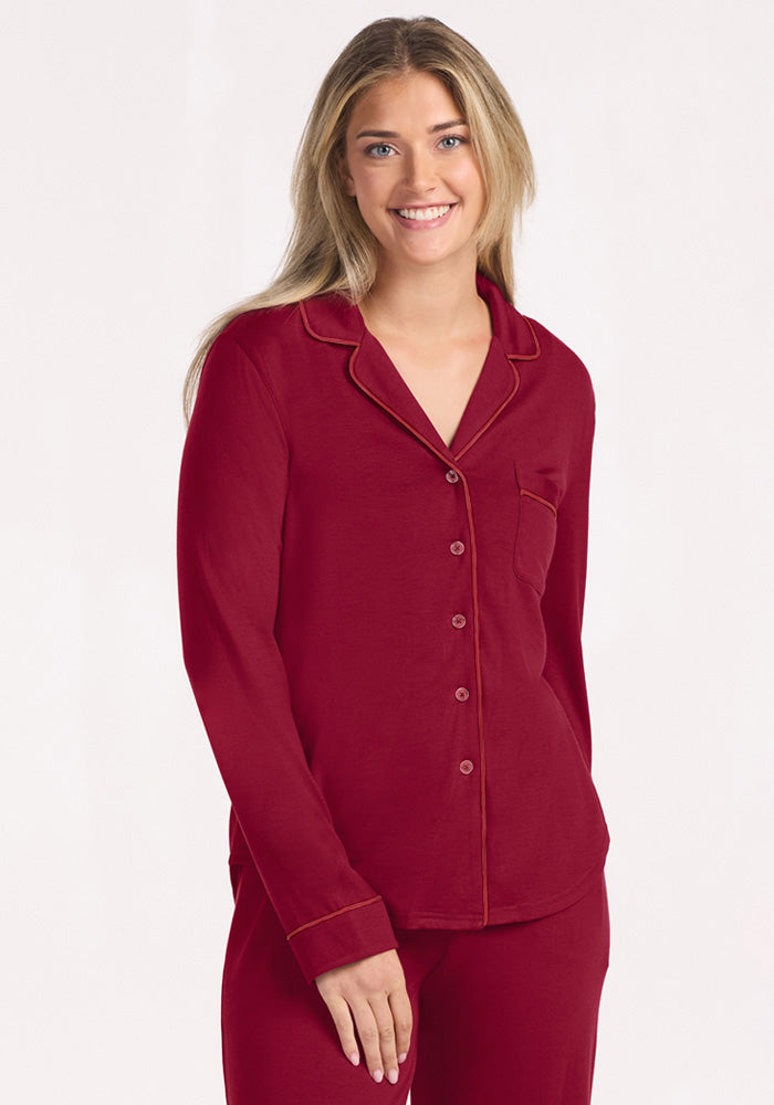 A woman smiles in a beet red Harper FeatherTouch® Pajama Set, featuring long sleeves, a button-down front, and piping.