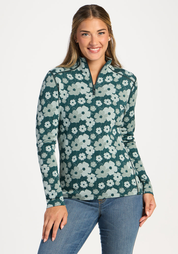 Woman smiles in Woolx Emi 1/4 Zip - Coastal Wildflower pullover and blue jeans against a plain white background. 