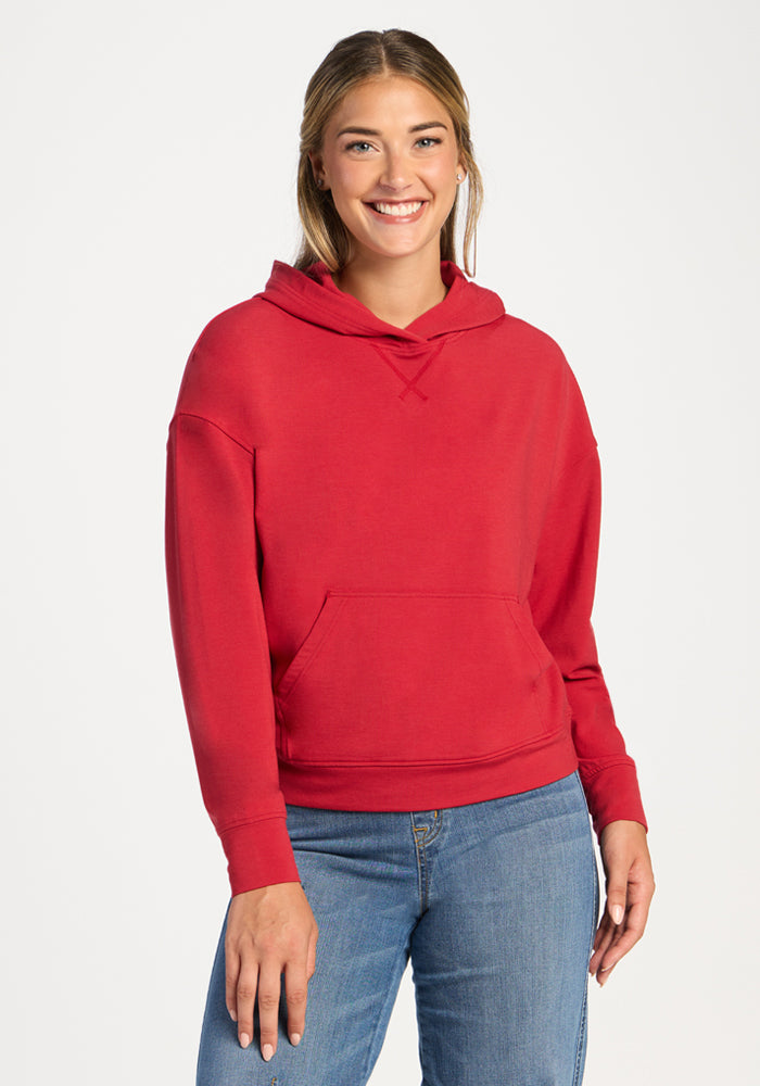 Smiling woman in a Woolx Lizzy Hoodie - Maraschino Cherry and blue jeans stands against a white background. 