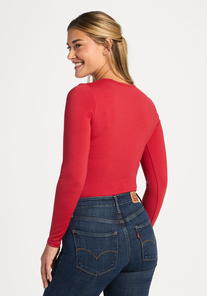 Woman smiles in Woolx Margot Bodysuit - Maraschino Cherry, red top and jeans, back to camera.