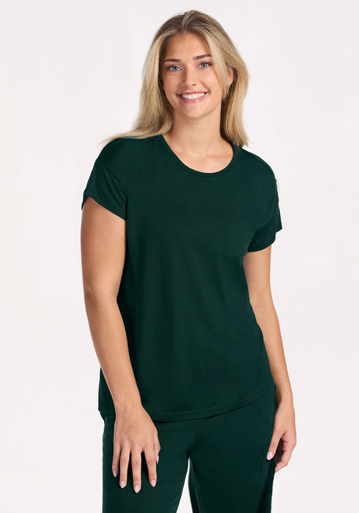 A smiling woman wears a dark green, moisture-wicking merino wool Billie Lounge Tee - Deep Pine. | Ariana is 5'11", wearing a size S