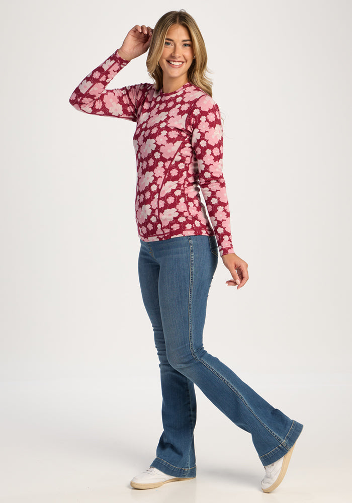 Woman in Woolx Maddie Baselayer Top - Floral Crush, blue jeans, and white shoes poses against a white background.