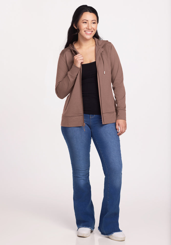 Smiling woman in Woolx Ryann Hoodie - Toasted Almond, black top, and blue jeans—a perfect travel essential look.