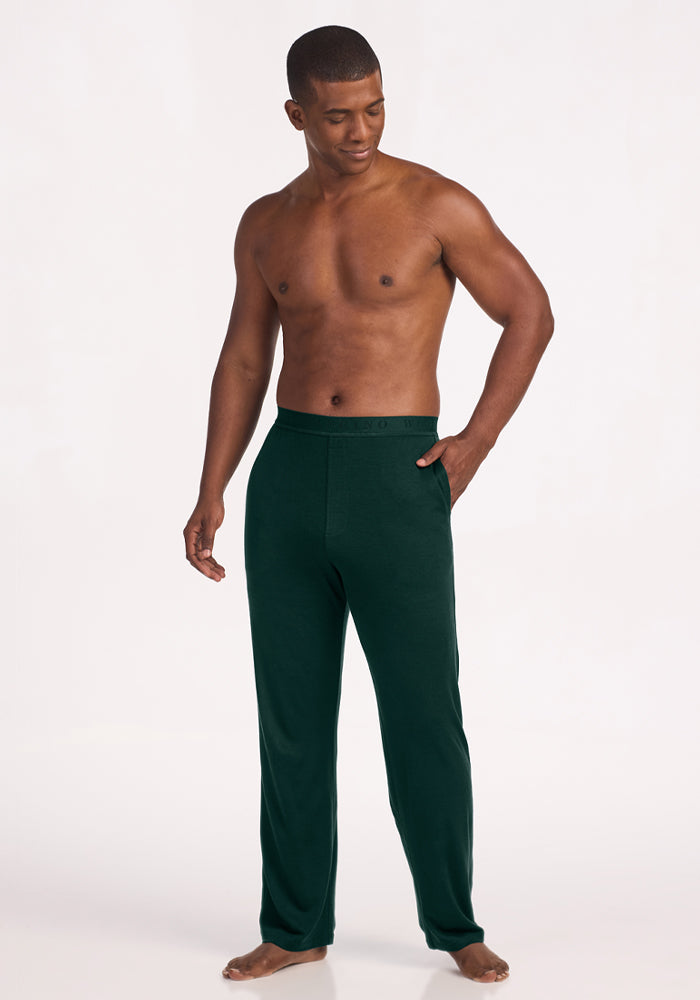 A shirtless man wearing deep pine Arlo Lounge Pants in lightweight merino wool with side pockets.