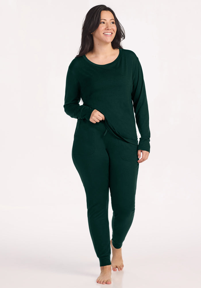 A woman wearing a dark green moisture-wicking long-sleeved shirt and Woolx Mary Kate Lounge Pants - Deep Pine.