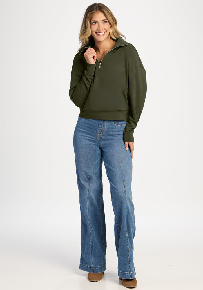 A woman wears an olive green Woolx Tori 1/4 Zip pullover with a quarter-zip and wide-leg blue jeans.