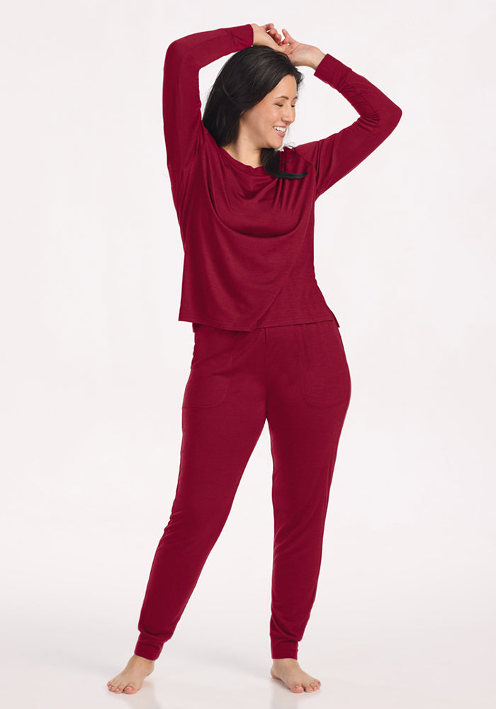A woman with arms raised above her head wears a wrinkle-resistant, Merino wool Ashlie Lounge Top in Beet Red.
