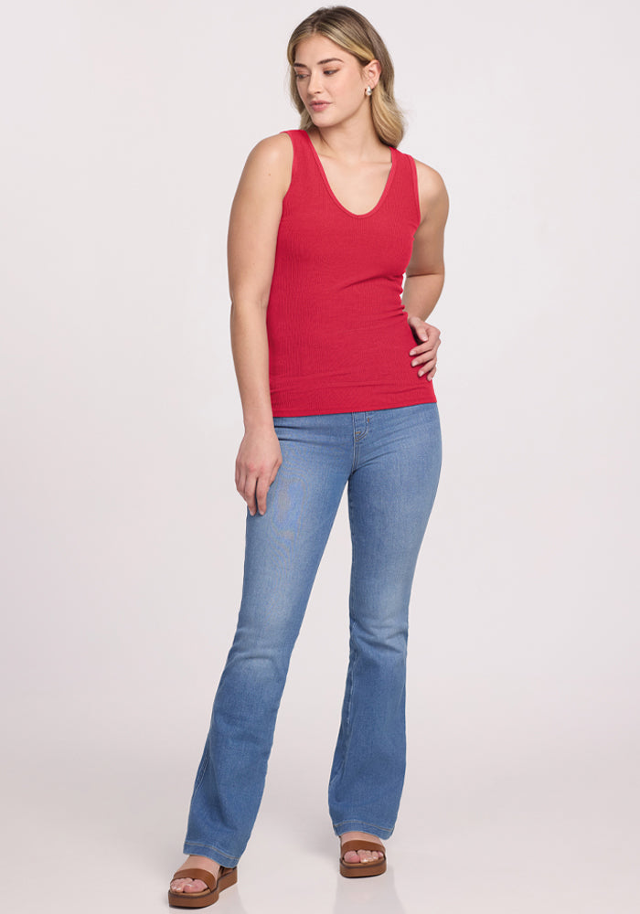 Woman wears Woolx Vivi Ribbed Tank in Berry Ice Pop, blue jeans, and brown sandals against a plain light background.