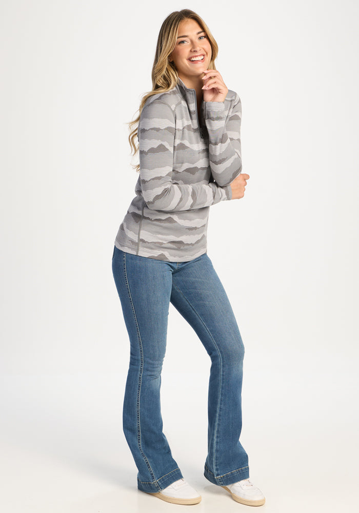 Woman in Woolx Emi 1/4 Zip - High Peaks poses in blue jeans, hand near chin, against a white background.