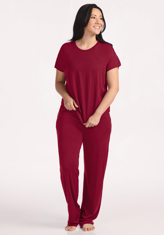 A woman smiles in a deep red Billie Lounge Tee and matching moisture-wicking merino wool lounge pants.