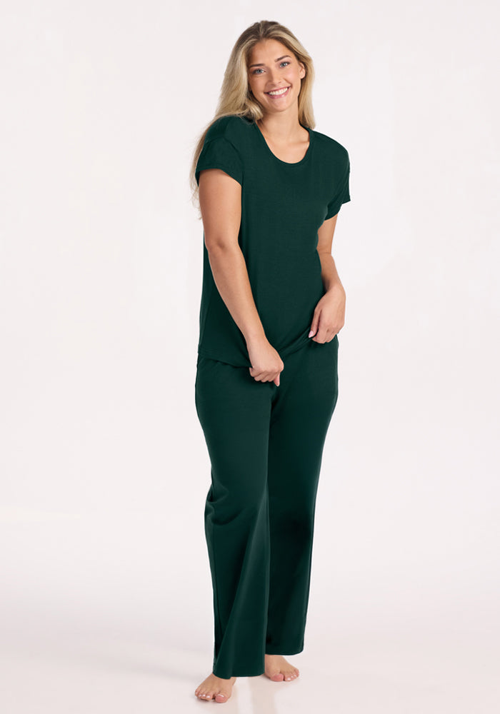 A smiling woman wears a dark green Billie Lounge Tee - Deep Pine and matching lounge pants.
