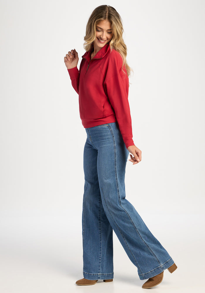 A woman wears a Maraschino Cherry Woolx Tori 1/4 Zip, wide-leg blue jeans, and brown ankle boots.