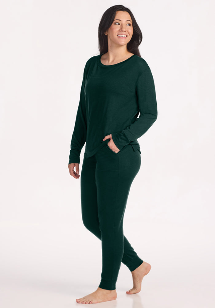 A woman wearing a deep pine Woolx Ashlie Lounge Top and matching wrinkle-resistant joggers with pockets.