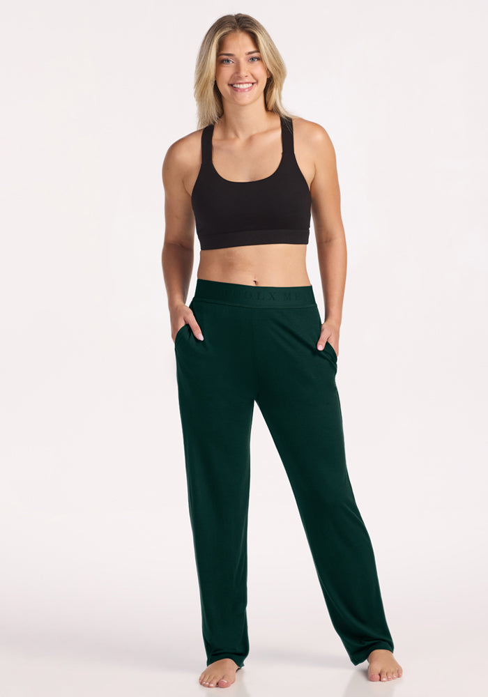 A woman wears a black sports bra and Deep Pine Woolx Maya Lounge Pants with pockets.