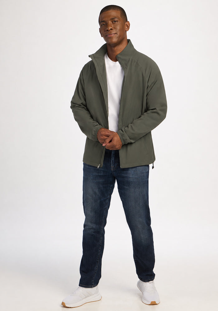 A man wearing a sage olive Woolx Dominator Windbreaker over a white t-shirt and blue jeans.