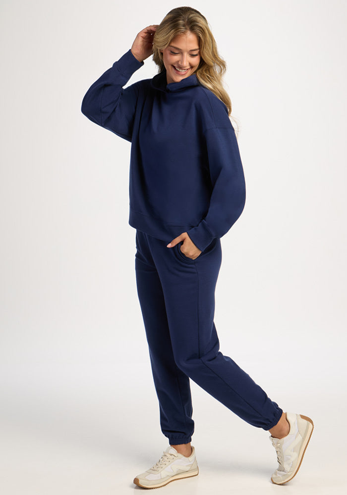 A woman wearing a dark blue Woolx Genevieve Hoodie - Ocean Cavern, matching sweatpants, and white sneakers.
