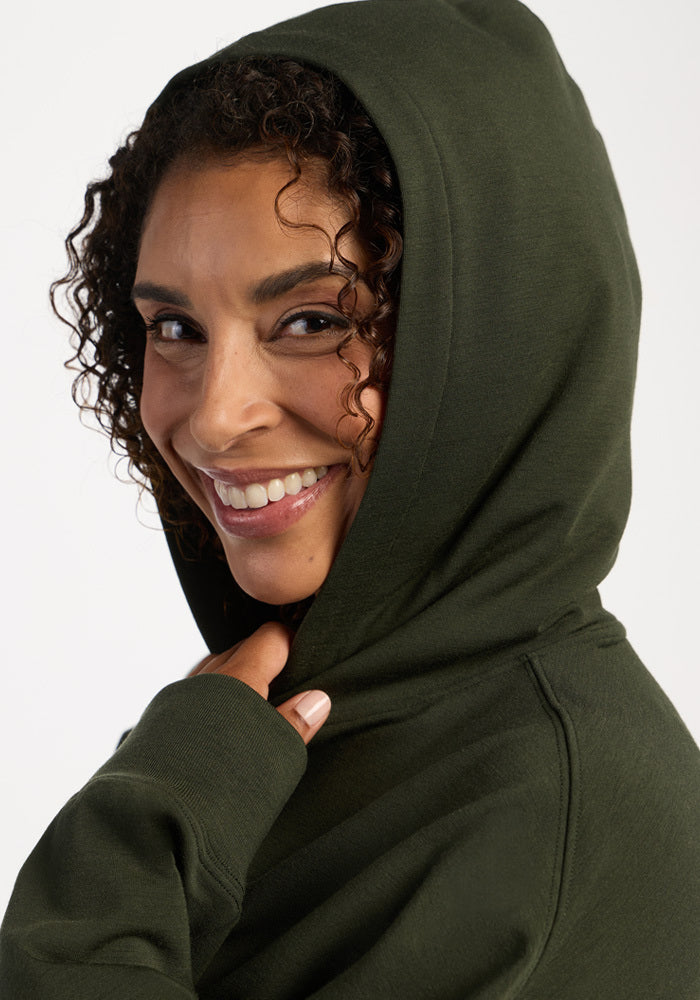 Smiling woman wearing a dark green Genevieve Hoodie - Duffel Bag in moisture-wicking merino wool.