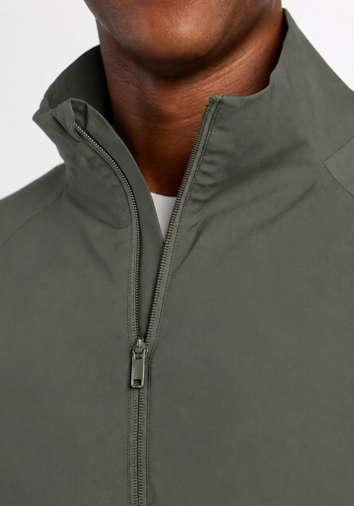 Close-up of a person wearing a sage olive Woolx Dominator Windbreaker with a high neck and front zipper.