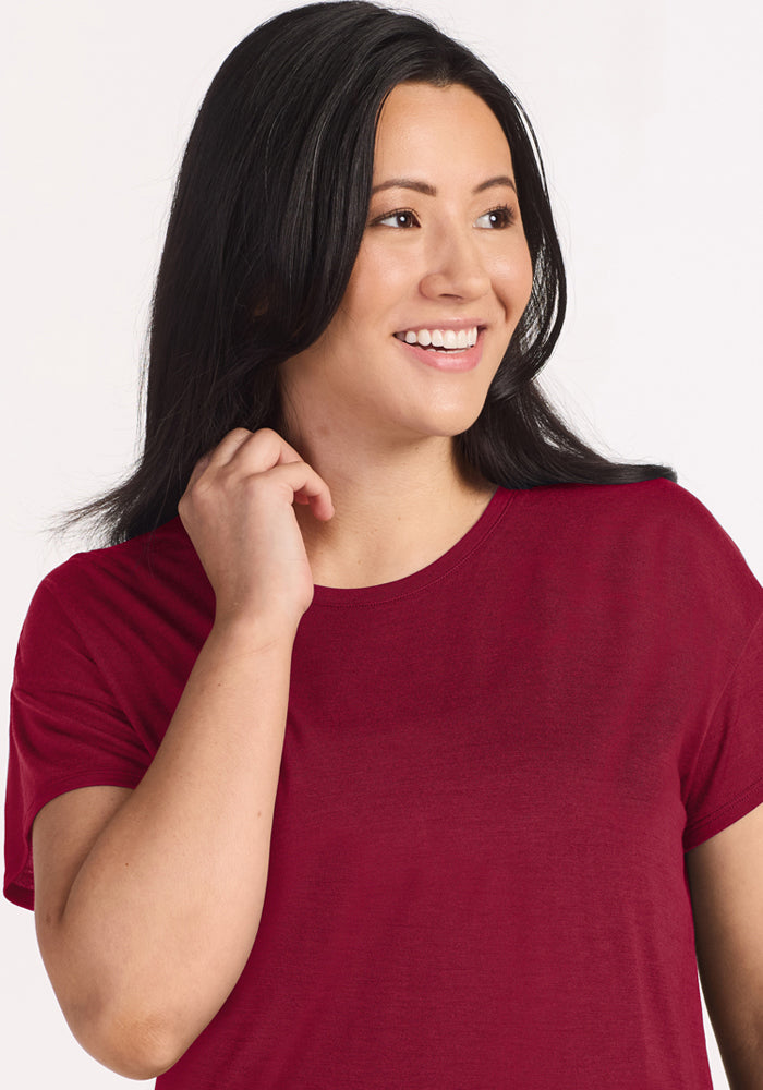 A woman smiles wearing a moisture-wicking, beet red Woolx Billie Lounge Tee.