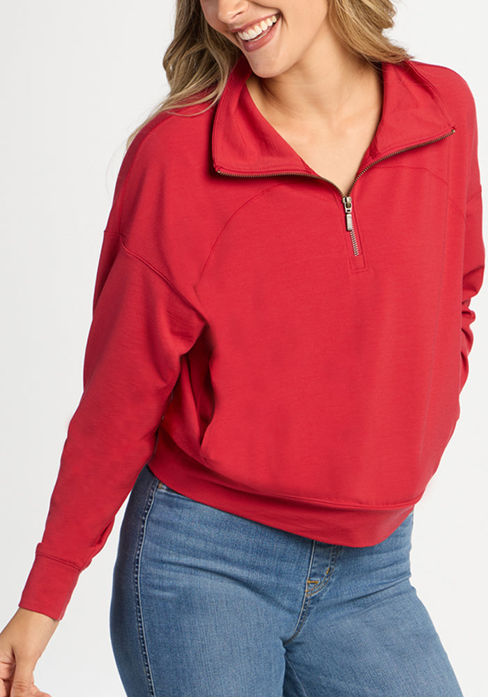 A person wears a Maraschino Cherry Woolx Tori 1/4 Zip pullover with a high collar and blue jeans.