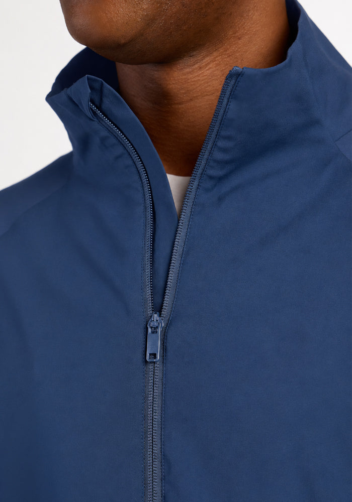 Close-up of a person wearing a dark blue Woolx Dominator Windbreaker - Vintage Indigo with a high collar.