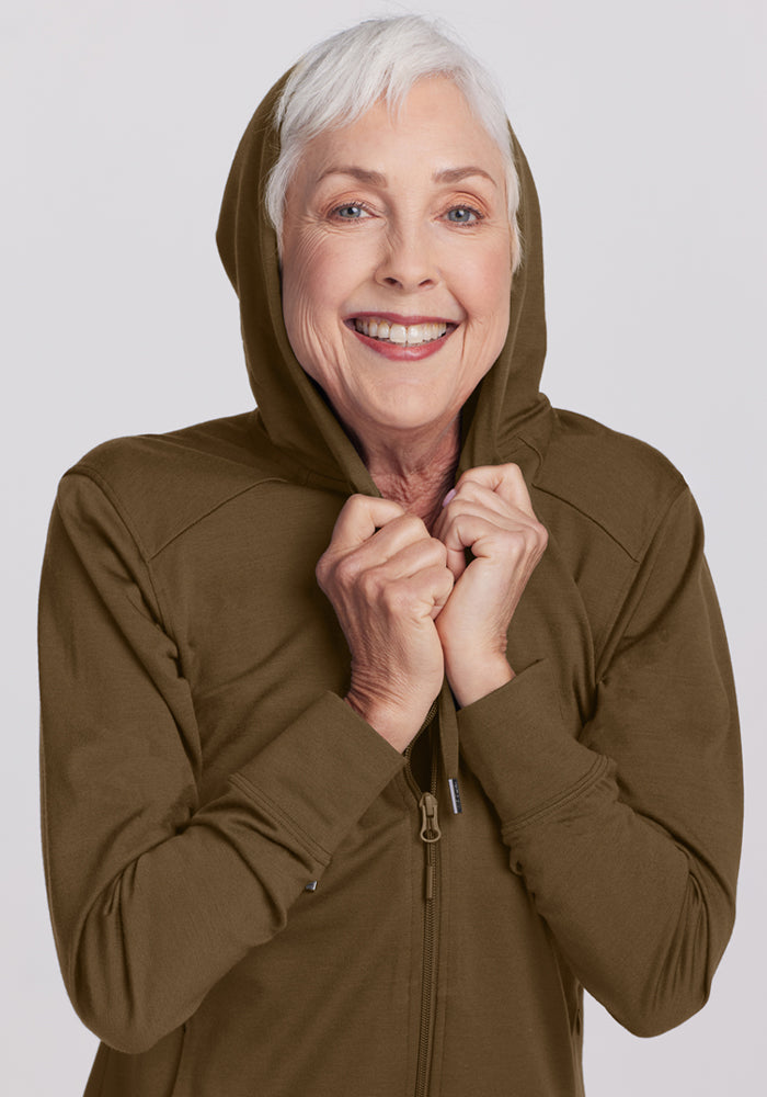 Smiling older woman in a Woolx Ryann Hoodie - Olive Leaf holds the hood—her must-have travel essential.