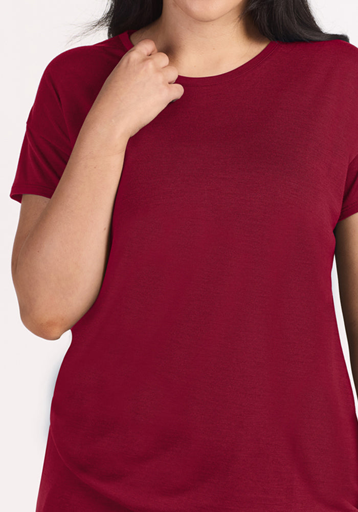 A person wearing a short-sleeved dark red moisture-wicking Merino wool Billie Lounge Tee - Beet Red crewneck t-shirt.