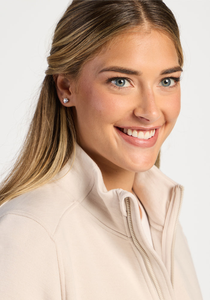 A smiling woman wearing an ecru Woolx Teddy Sweatshirt, an ultra-heavyweight merino wool zip-up mock neck.