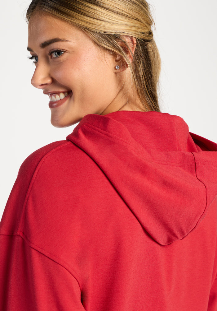 Smiling woman in the Woolx Lizzy Hoodie - Maraschino Cherry, shows off its buttery soft Meriluxe fabric and hood.