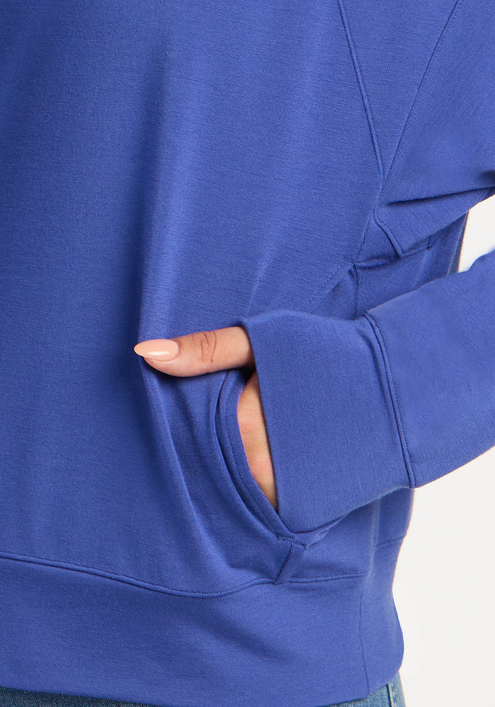 Close-up of a royal blue Woolx Tori 1/4 Zip merino pullover with a hand resting in a side pocket.