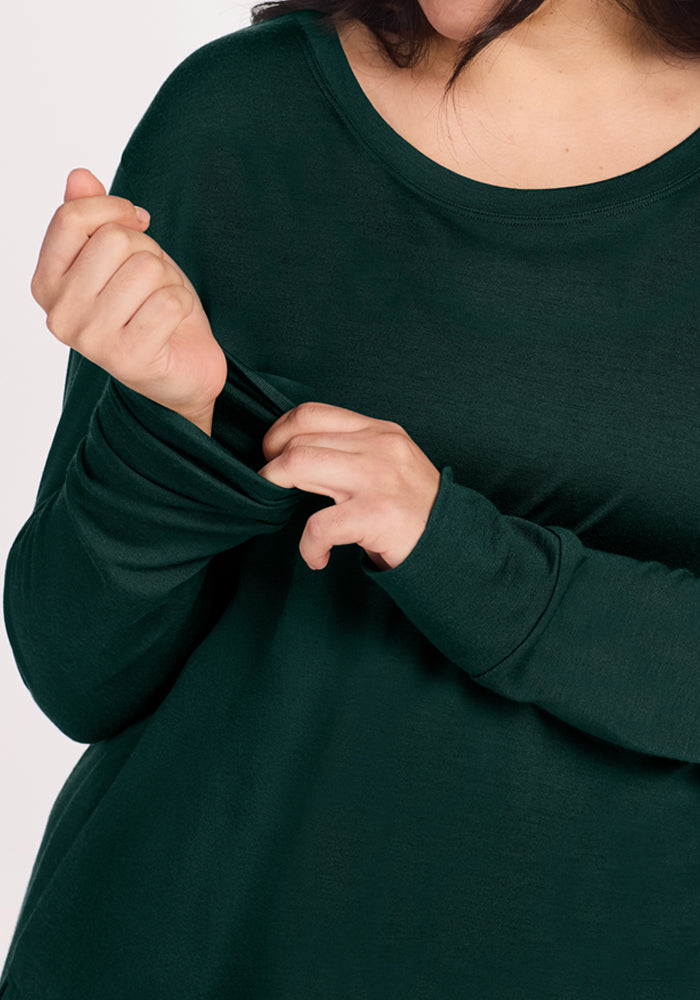 A person pulls at the sleeve of their Deep Pine Ashlie Lounge Top, a dark green, wrinkle-resistant merino wool travel top.
