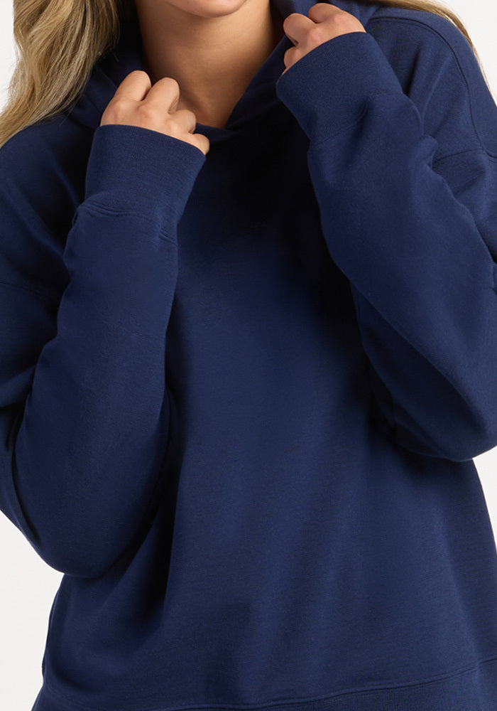 A person pulls the hood of their Ocean Cavern Genevieve Hoodie up with both hands.