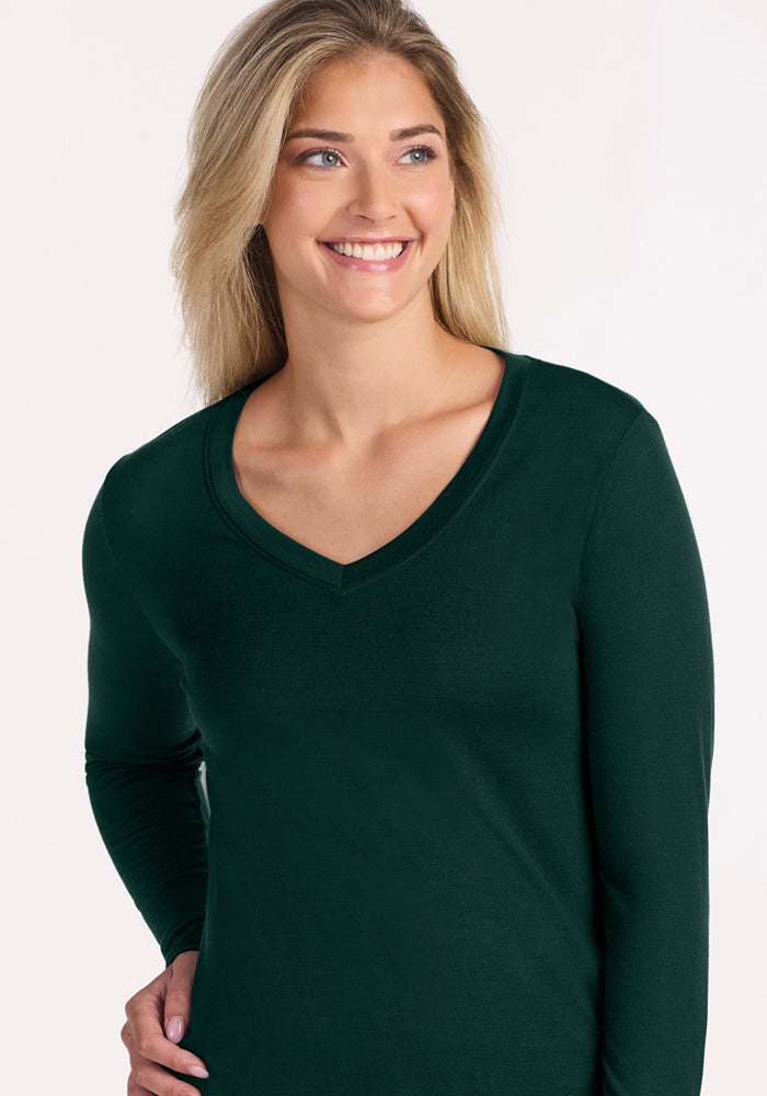 A smiling woman wears a dark green, long-sleeved Woolx Lily V Neck Lounge Top in Deep Pine.