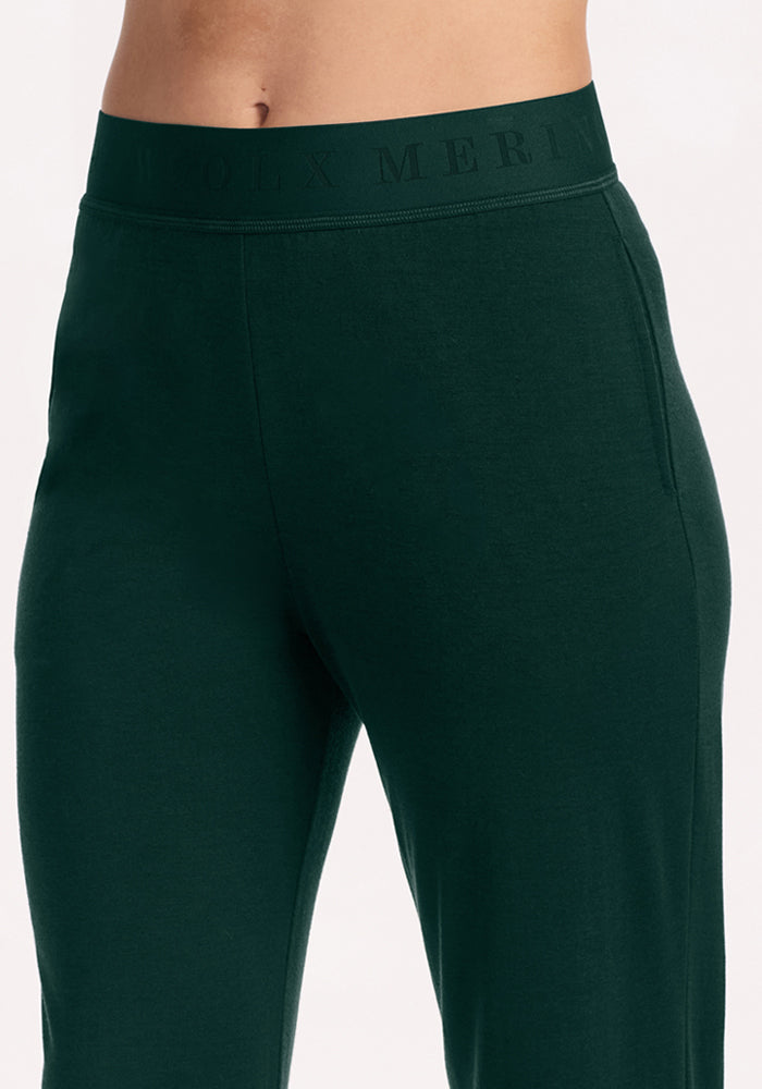 Woolx Maya Lounge Pants in Deep Pine, a dark green moisture-wicking style with a tonal text elastic waistband.