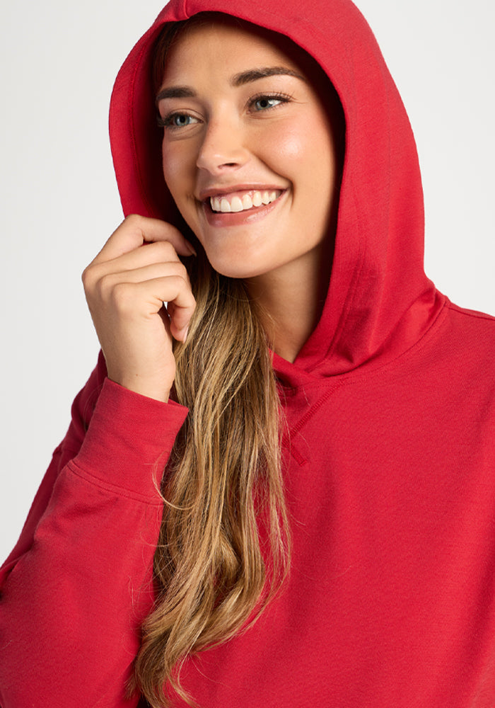 Smiling woman in the Woolx Lizzy Hoodie - Maraschino Cherry, holding the hood and looking to the side.