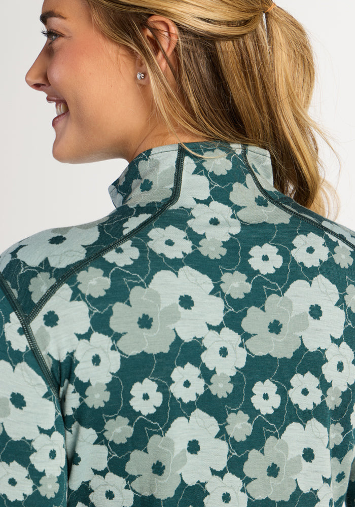 Woman smiling, shown side and back, wears Woolx Emi 1/4 Zip—Coastal Wildflower over a Merino wool base layer.