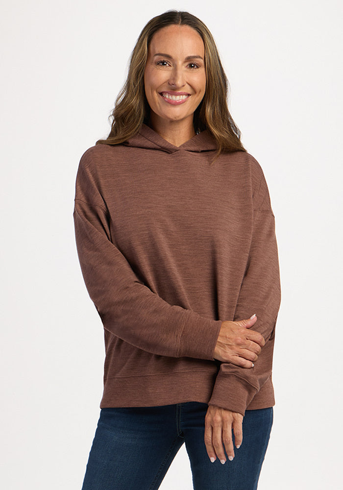 A smiling woman wears a long-sleeved brown Genevieve Hoodie - Sable Heather and blue jeans.