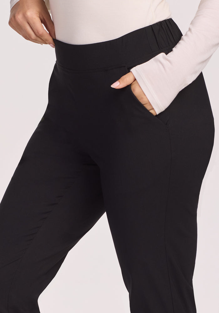 A person stands with one hand in their pocket, wearing a long-sleeve cream top with thumb holes and Woolx Nicole Petite Pants in black. The image is cropped to show only the torso and upper legs.
