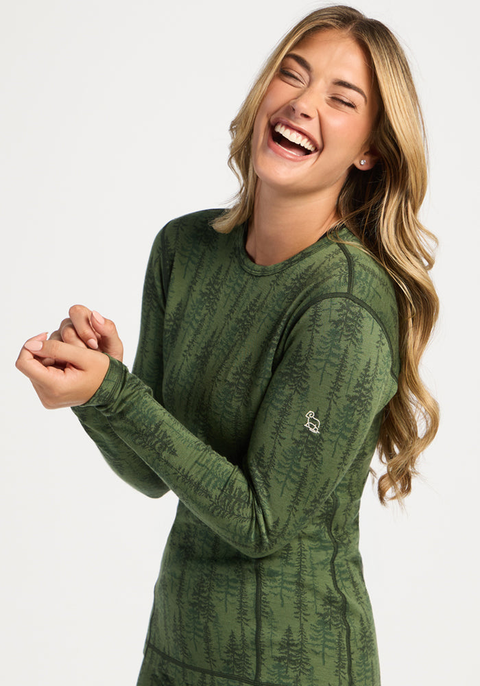 Woman with long hair laughing in a Woolx Maddie Baselayer Top - Forest Friends, dark tree pattern, light background.