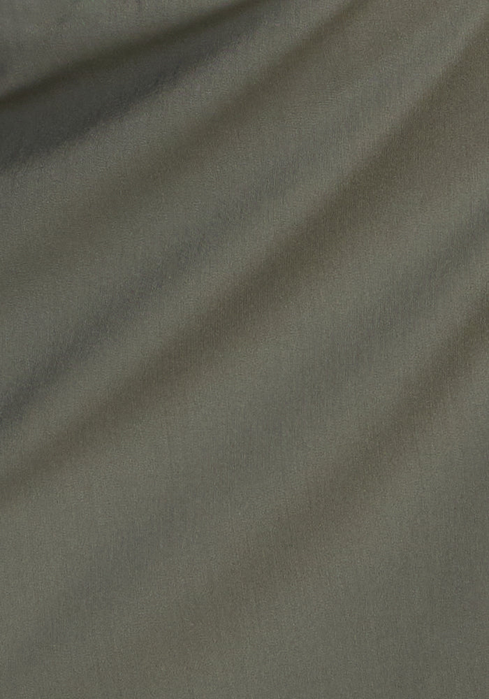 Close-up of sage olive fabric on the Woolx Topanga Skort, showing soft, diagonal folds and subtle texture. Lighting highlights gentle shadows and creases across this moisture-wicking merino wool activewear material.