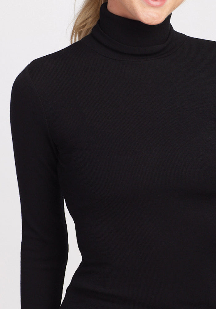 Person wears Woolx Sage Petite Ribbed Turtleneck in black, face partly visible, against a plain light background.