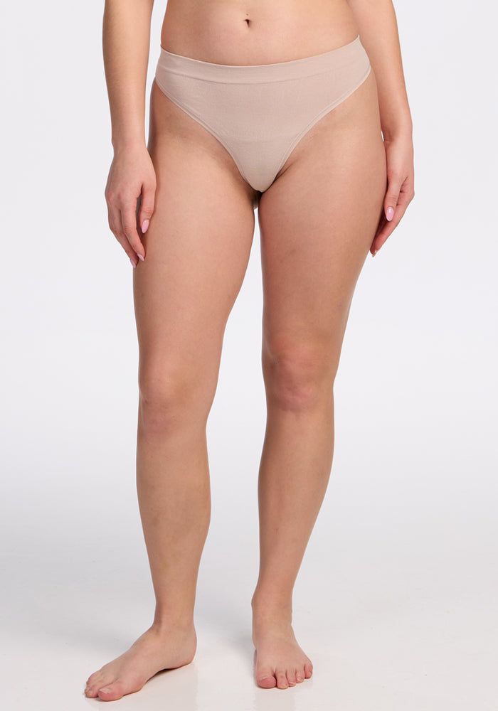 A person stands barefoot against a white background, wearing the Woolx Farrah Thong in Sand. The high-cut seamless underwear offers a smooth, comfortable fit, shown in a cropped image from the shoulders down.