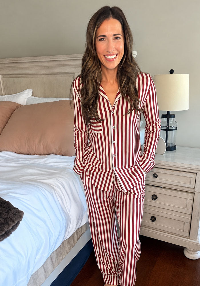 A woman smiles in a Woolx Harper FeatherTouch® Pajama Set, featuring moisture-wicking red and white vertical stripes.