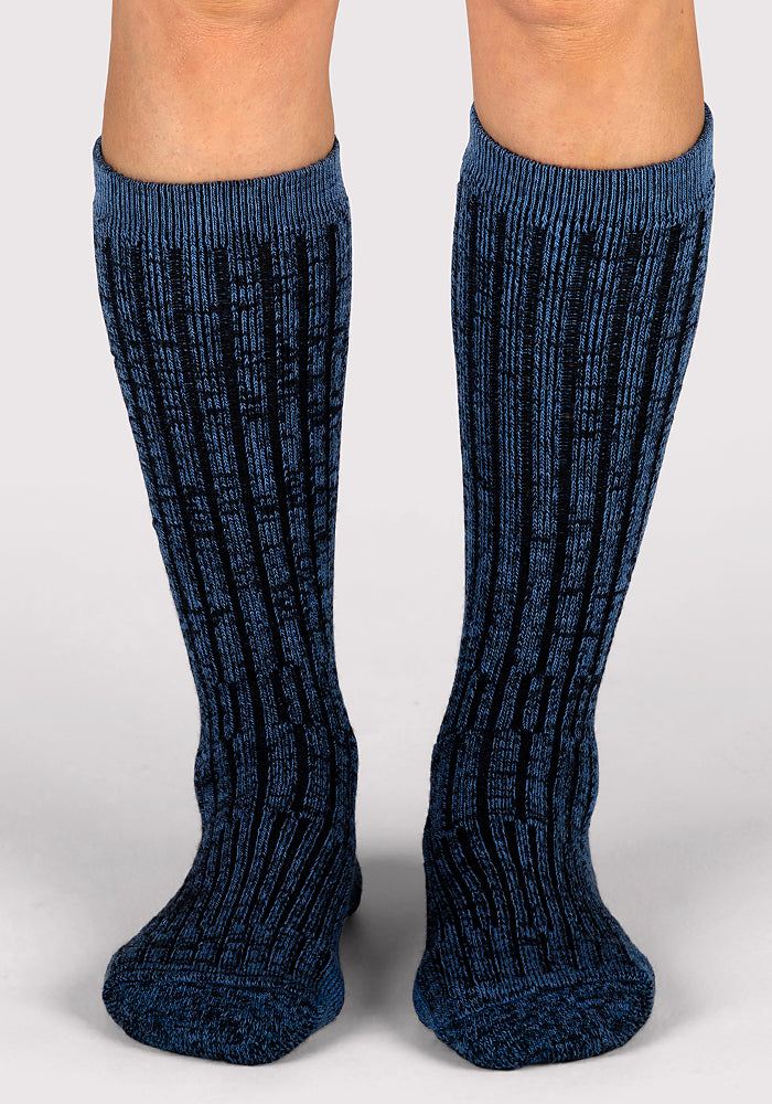 A pair of legs wears Woolx Womens Joey Mid Calf Socks in Steel Blue, featuring a ribbed design, standing on a plain light gray background.