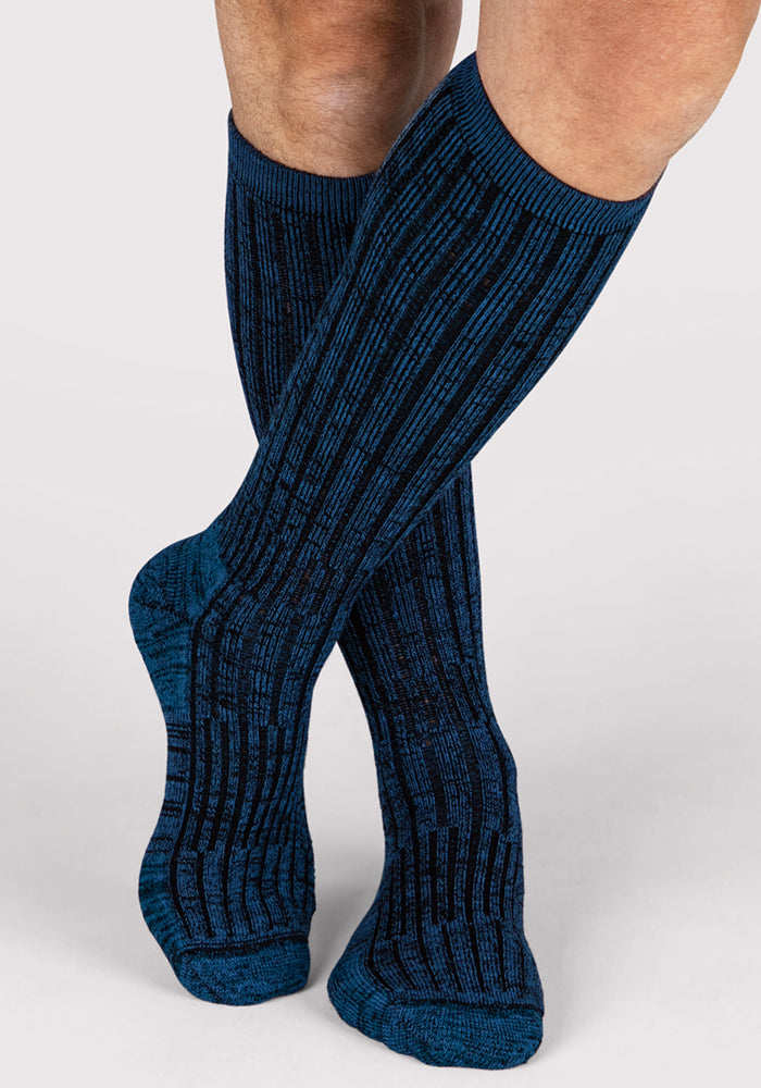 A man wearing Woolx Mens Joey Mid Calf Socks in Steel Blue stands with one leg crossed over the other against a plain light background.
