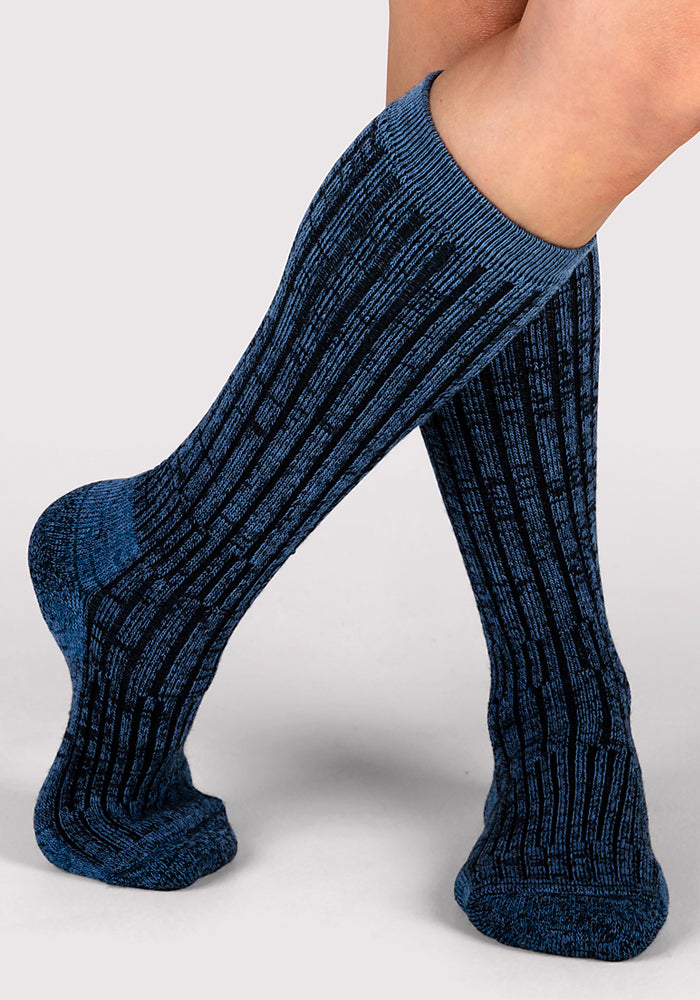 A person with crossed legs wears Woolx Womens Joey Mid Calf Socks in Steel Blue, shown against a light gray background.