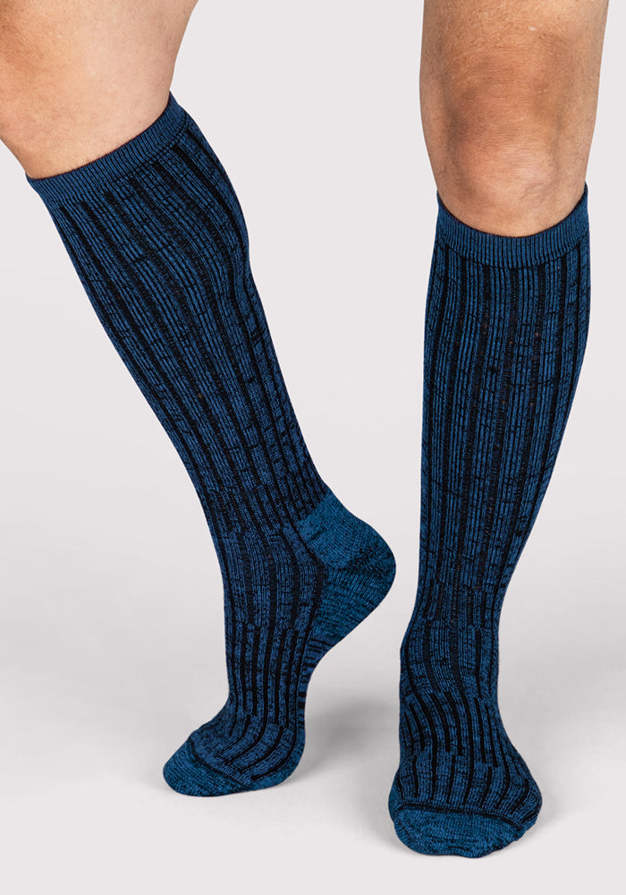 A pair of legs wearing Woolx Mens Joey Mid Calf Socks in Steel Blue, featuring a ribbed pattern, standing against a plain light gray background.