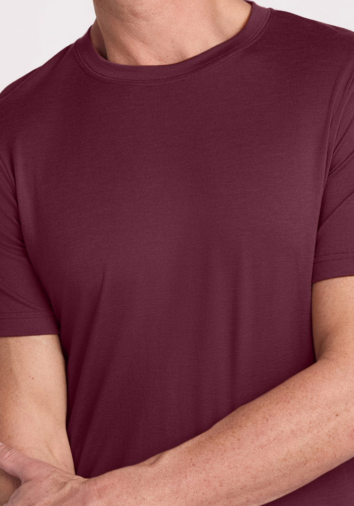 A person wearing the Woolx Endurance Tee in Grape Harvest (maroon), shown from shoulders to mid-torso with arms relaxed and one arm crossing over the other; their face is not visible.