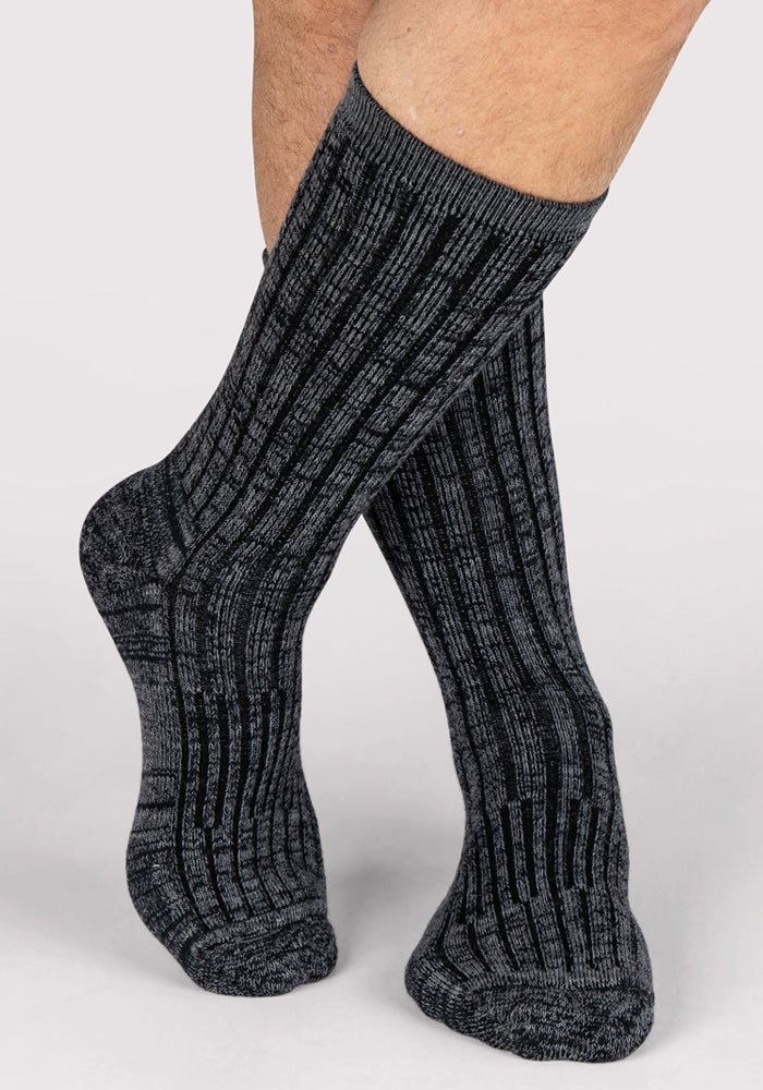 A person wearing Woolx Mens Joey Crew Socks in Stone Grey stands with one leg crossed over the other against a light background.