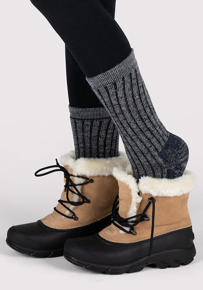 A person wearing Woolx Womens Joey Crew Socks, black leggings, and tan winter boots with black soles and faux fur trim stands against a plain light background.